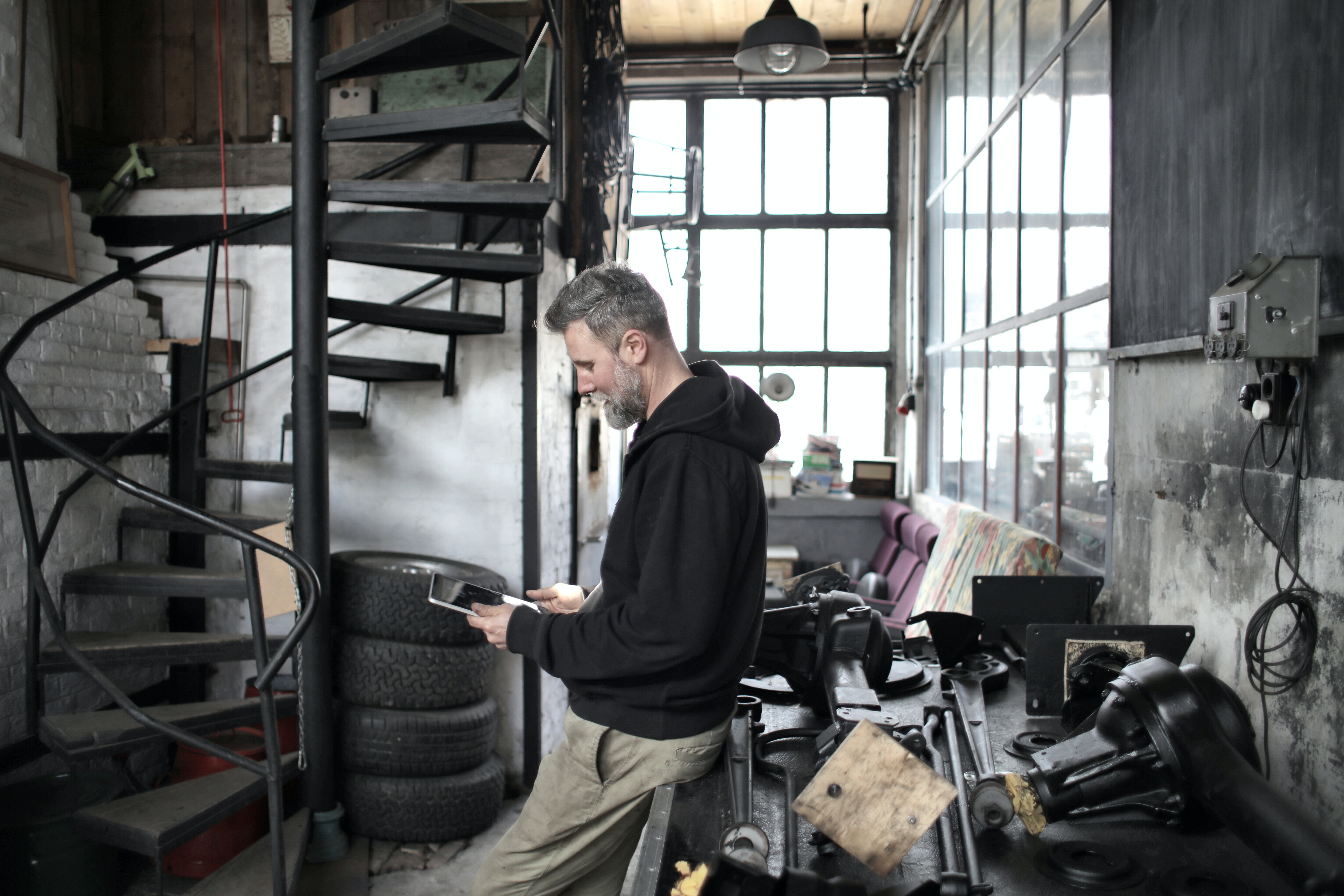 bearded-worker-using-tablet-while-standing-near-workbench-in-3823025